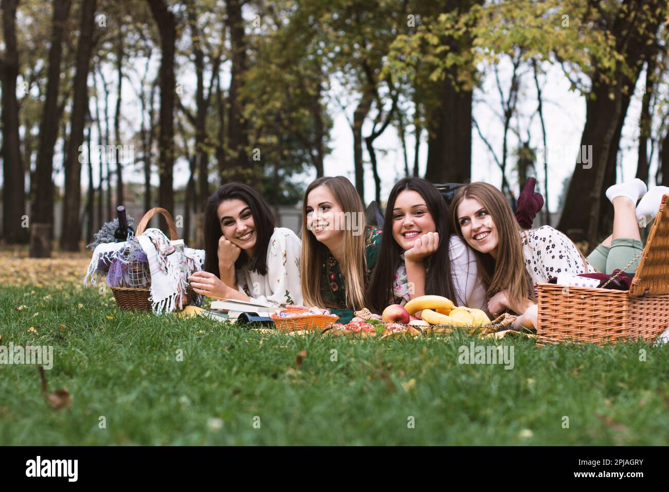 Eine Gruppe von vier Frauen auf einem lustigen Herbstpicknick im Park, die auf einer Decke liegen und sich amüsieren. Stockfoto