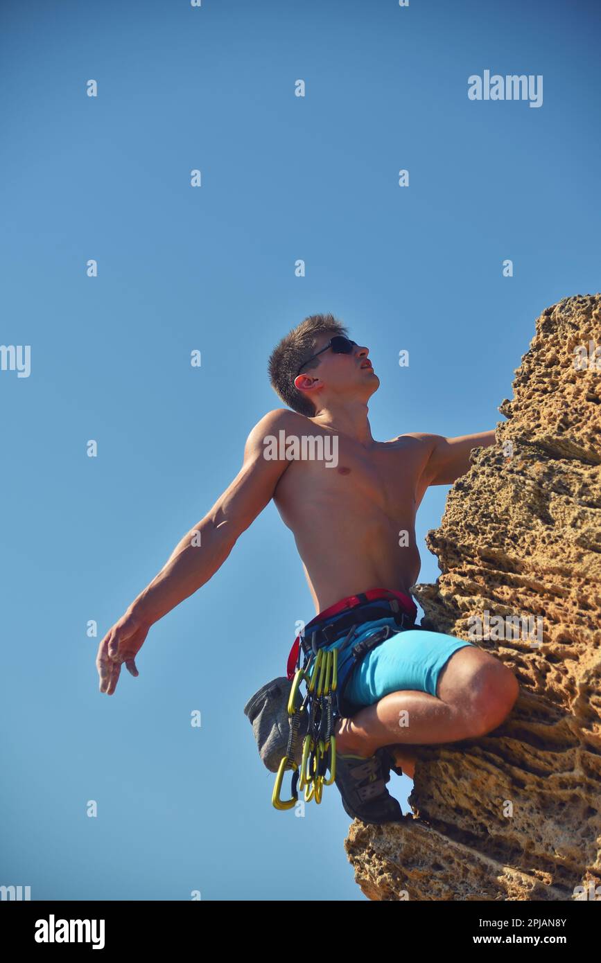 Rückansicht eines jungen männlichen Kletterers beim Klettern mit Karbinen Stockfoto