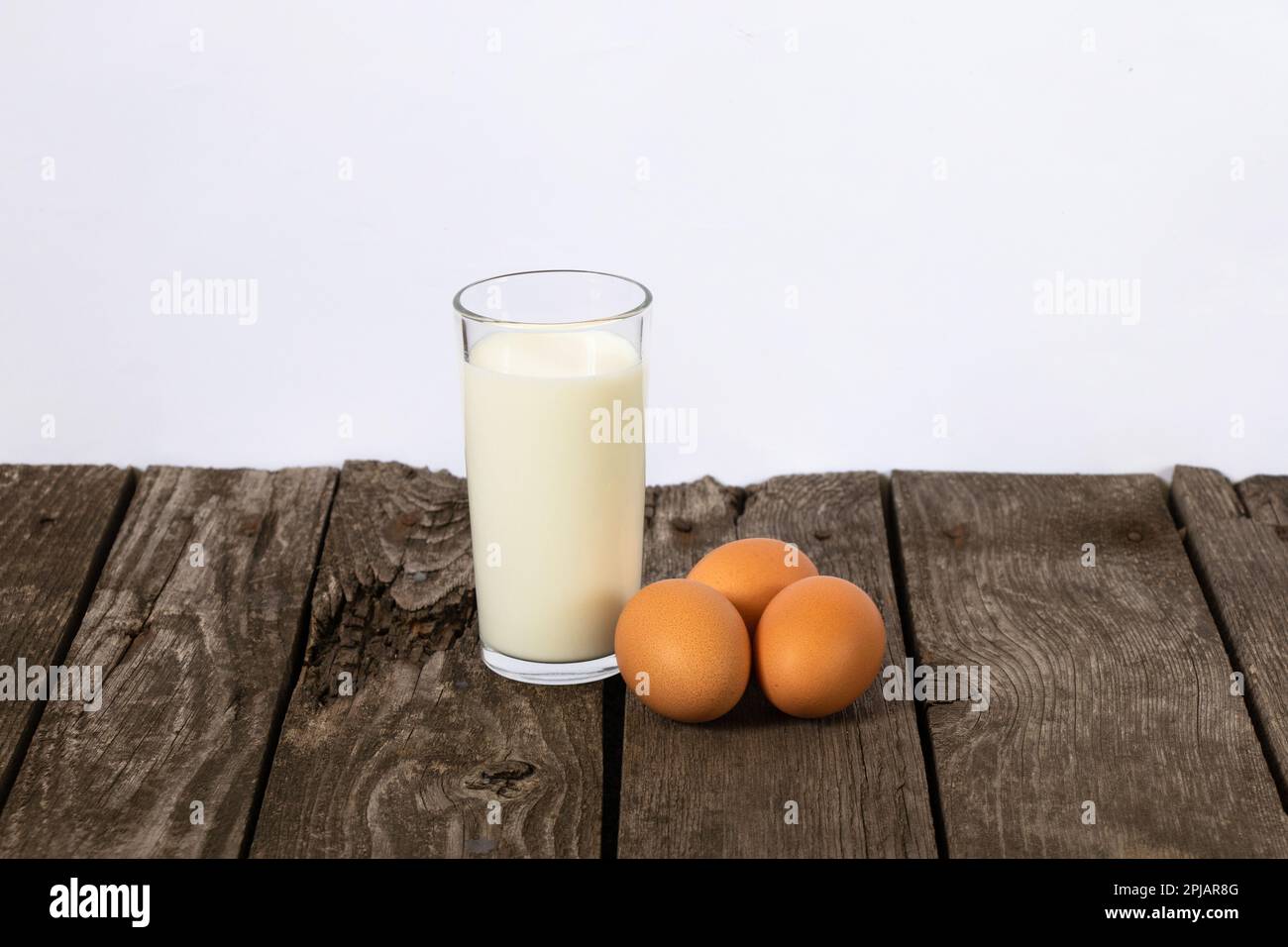 Ein Glas Milch und drei Hühnereier auf einem Tisch Stockfoto