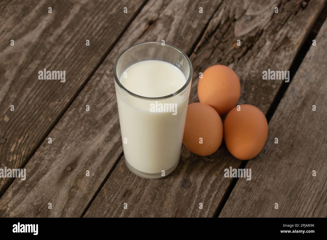 Ein Glas Milch und drei Hühnereier auf einem Tisch Stockfoto