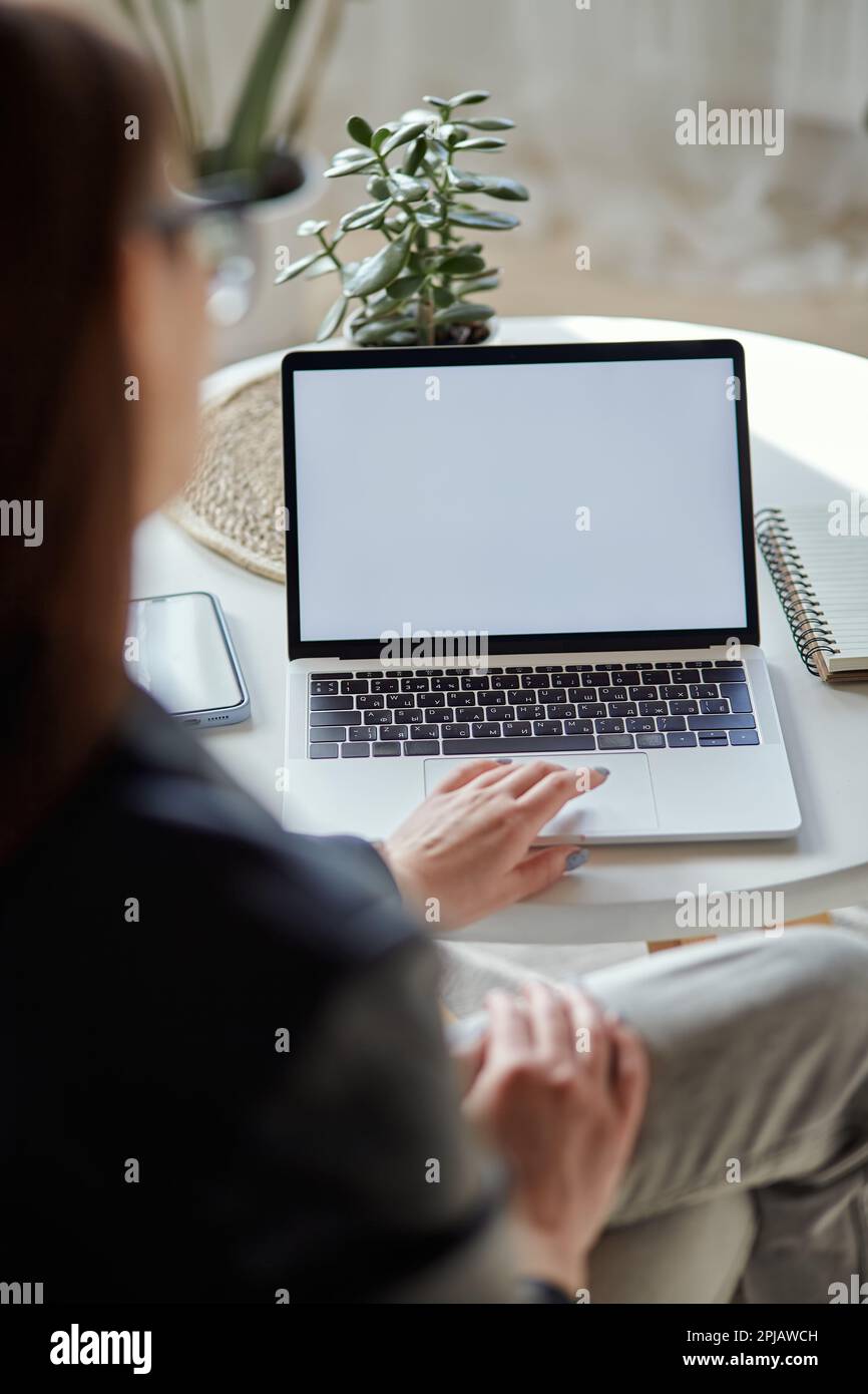 Modell eines weißen Laptops und einer Frau mit Handy, die zu Hause am Tisch sitzt, Rückansicht Stockfoto