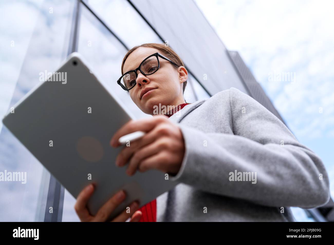 Selbstbewusste Frau mit Brille, die auf einem digitalen Tablet arbeitet. Stockfoto