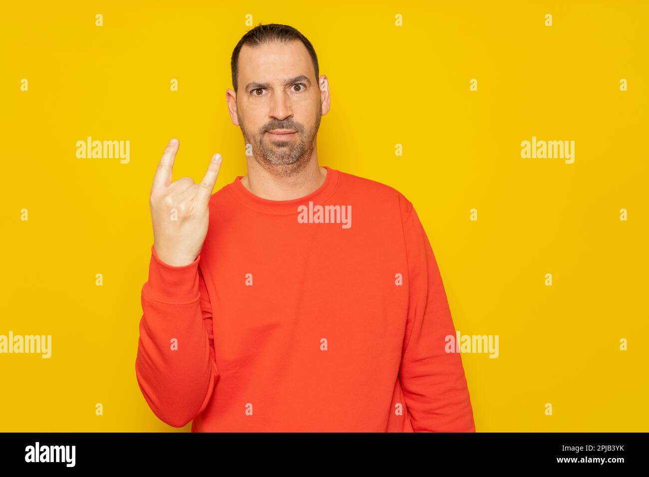 Ein gutaussehender Mann, der ein Sweatshirt auf einem isolierten gelben Hintergrund trägt, mit einem verrückten Ausdruck, der mit der Hand nach oben ein Rocksymbol macht. Music Star-Konzept. Stockfoto