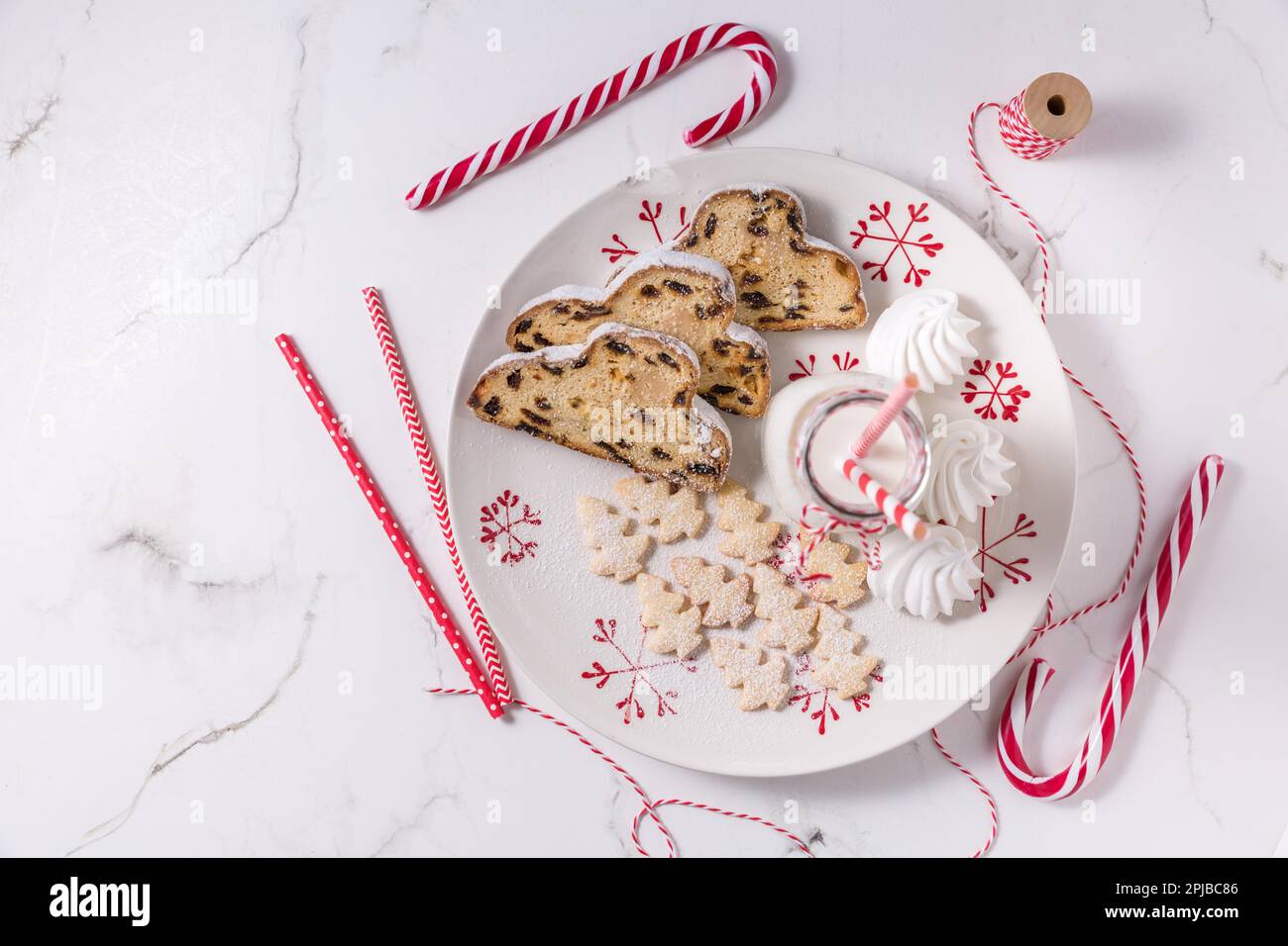 Flasche Milch mit traditionellem Weihnachtsstollen, kleinen Keksen und Zuckerrohr auf weißem Hintergrund. Deutsches Weihnachtsbrot Stockfoto