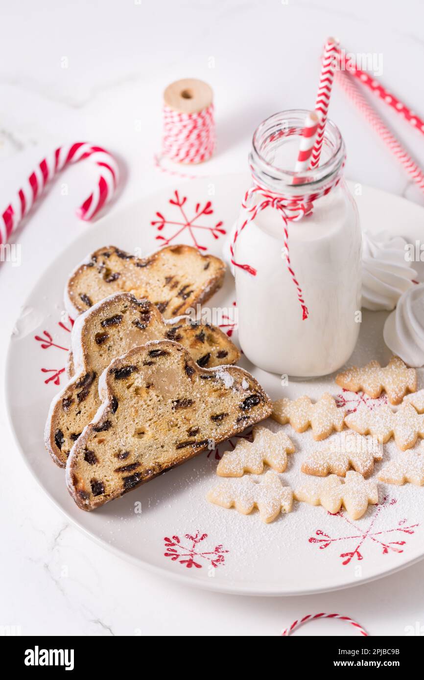 Flasche Milch mit traditionellem Weihnachtsstollen, kleinen Keksen und Zuckerrohr auf weißem Hintergrund. Deutsches Weihnachtsbrot Stockfoto