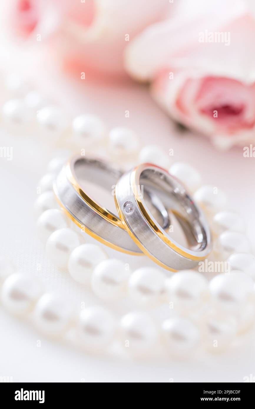 Moderne Eheringe mit Perlenkette mit rosa Rosen im Hintergrund, weicher Fokus Stockfoto