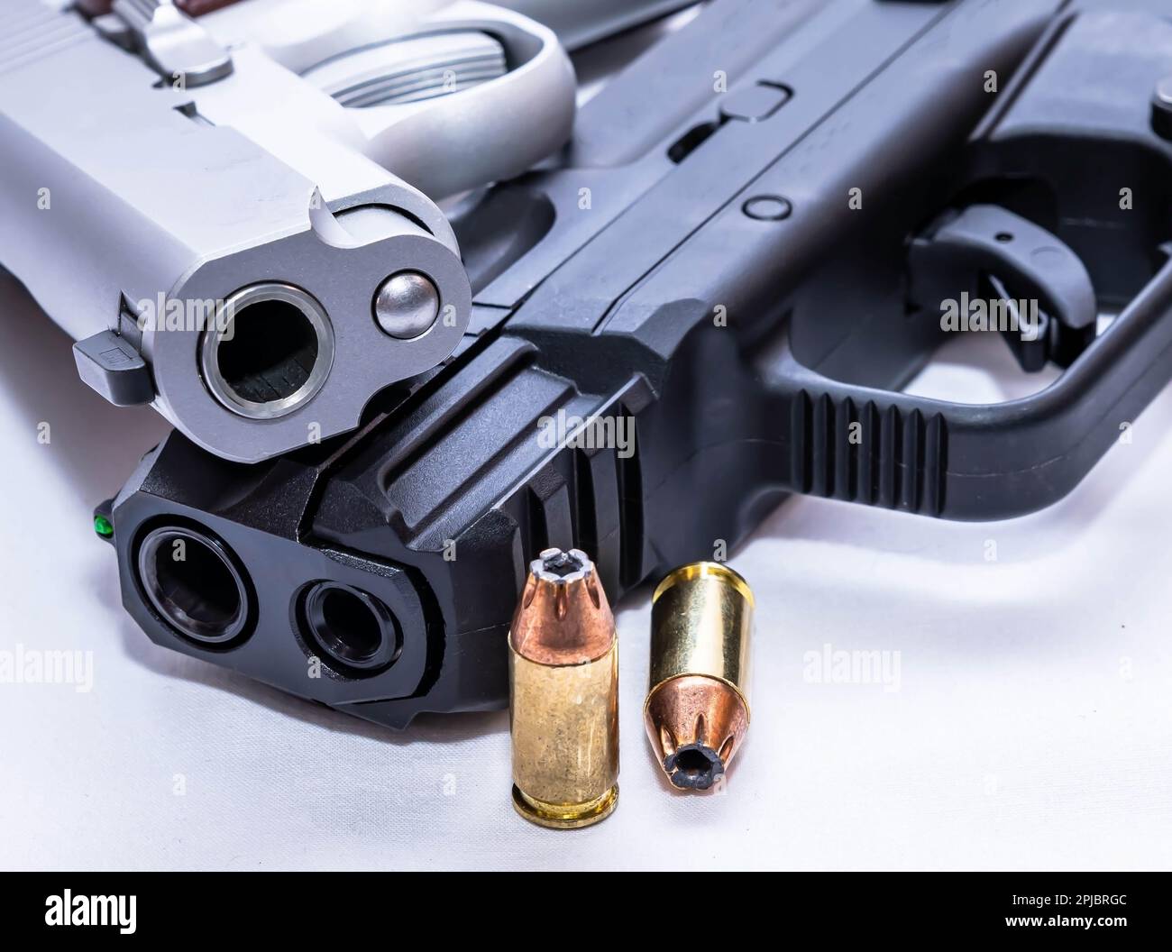 Zwei Pistolen, eine schwarz, der andere rostfrei, beide in einem Kaliber von 380 acp, mit zwei Hohlkugeln daneben auf weißem Hintergrund Stockfoto Zwei Pistolen, eine schwarz, der andere rostfrei, beide in einem Kaliber von 380 acp, mit zwei Hohlkugeln daneben auf weißem Hintergrund Stockfoto