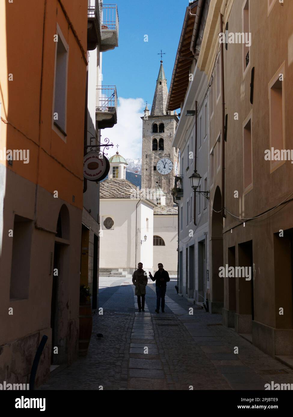 Männer in Silhouette gehen eine enge Straße hinunter in Richtung der Kathedrale Santa Maria Assunta in der Stadt Aosta, Aosta-Tal, Italien Stockfoto