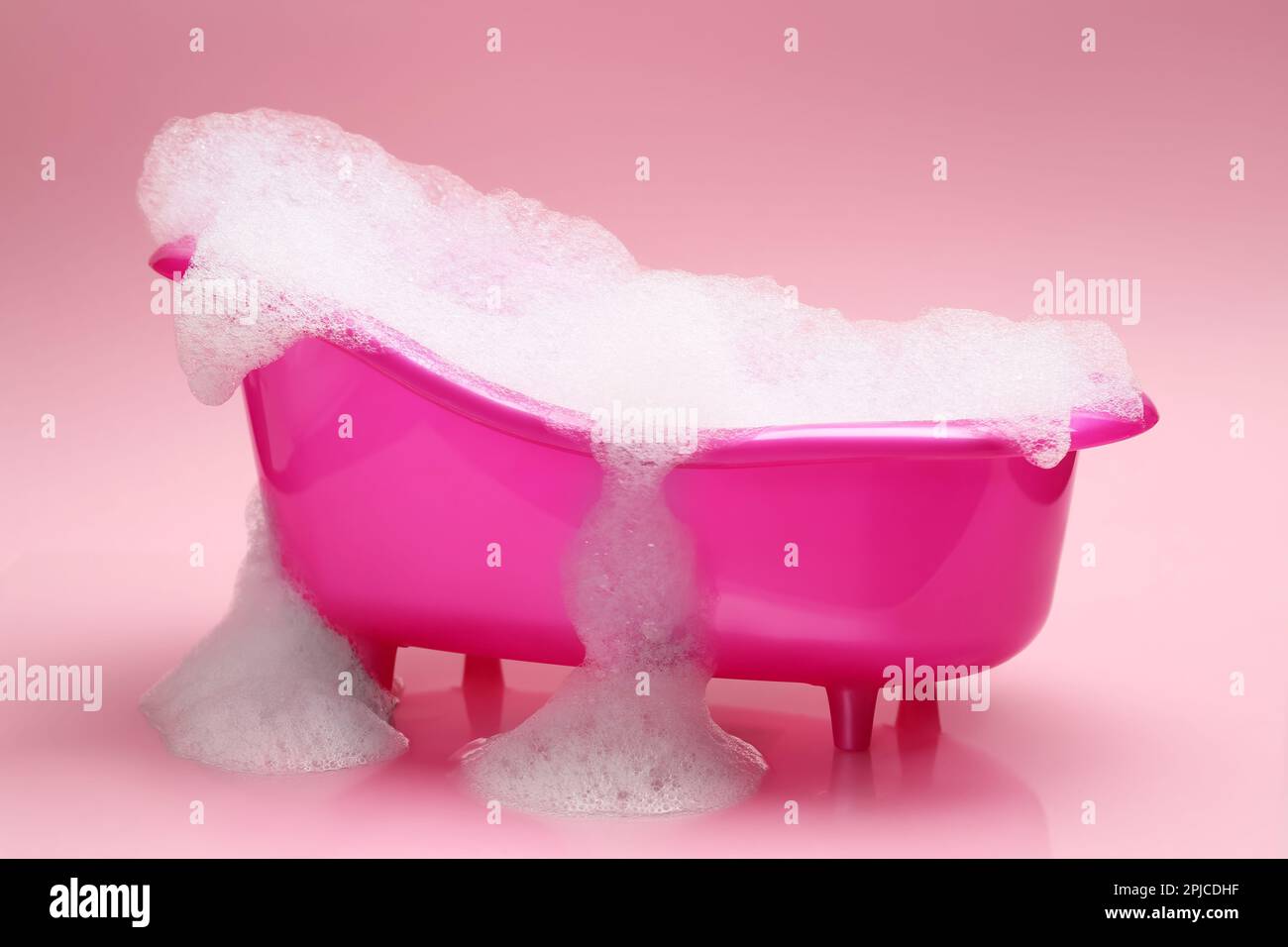 Spielzeugbadewanne mit Schaumstoff auf pinkfarbenem Hintergrund Stockfoto