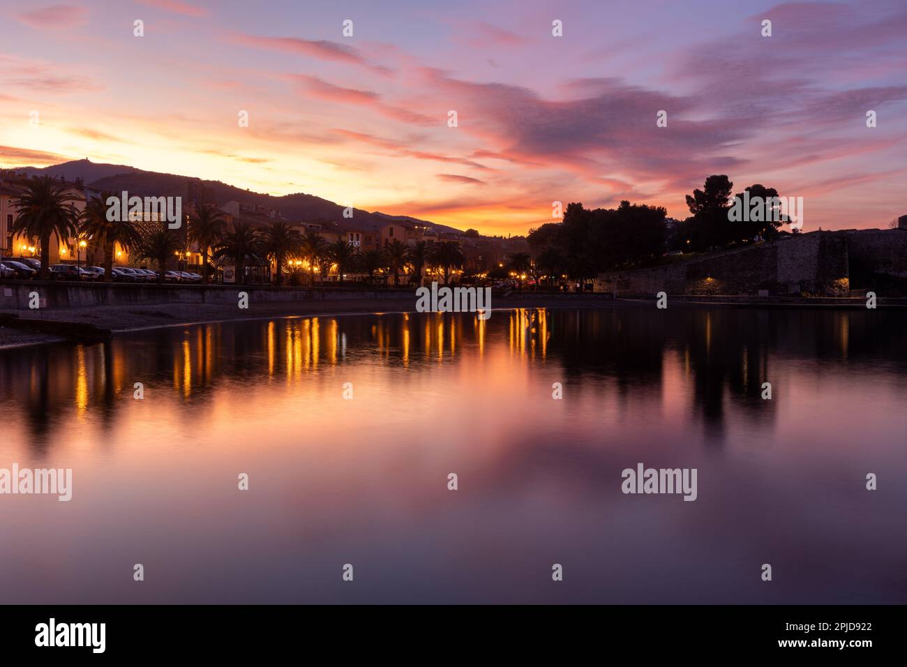 Der Blick auf die Stadt über das stille Wasser (Meer) in Coullioure, Frankreich nach dem Sonnenuntergang. Pink- und Violetttöne, der Himmel reflektiert sich im Wasser. Stockfoto