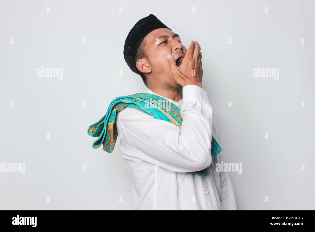 Lächelnder junger asiatischer Mann in einem muslimischen Hemd, der traditionelle Begrüßungen auf weißem Hintergrund trägt. Stockfoto