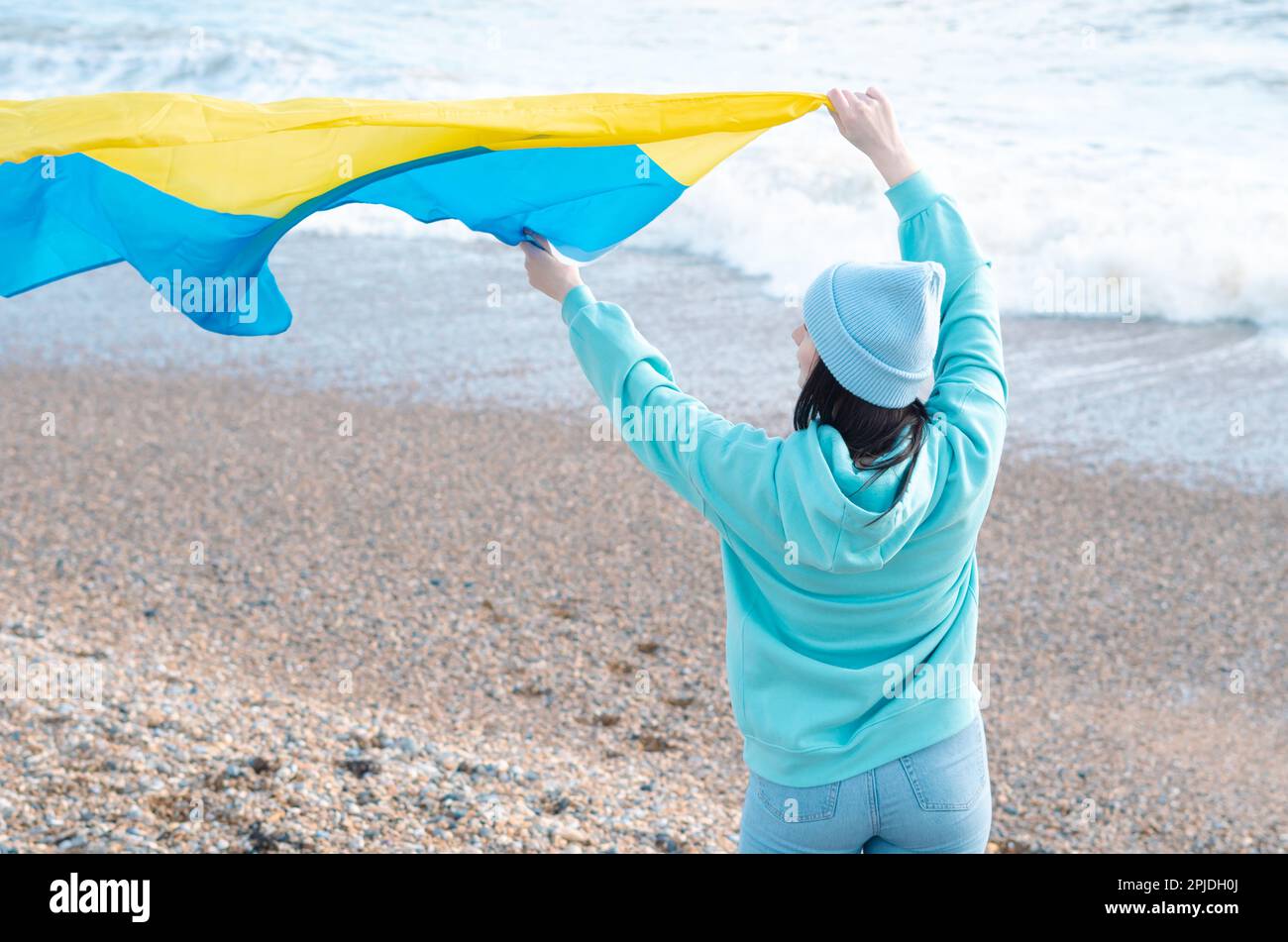 Braune Frau in blauem Hoodie und blauem Hut mit ukrainischer Nationalflagge, patriotisches Konzept Stockfoto