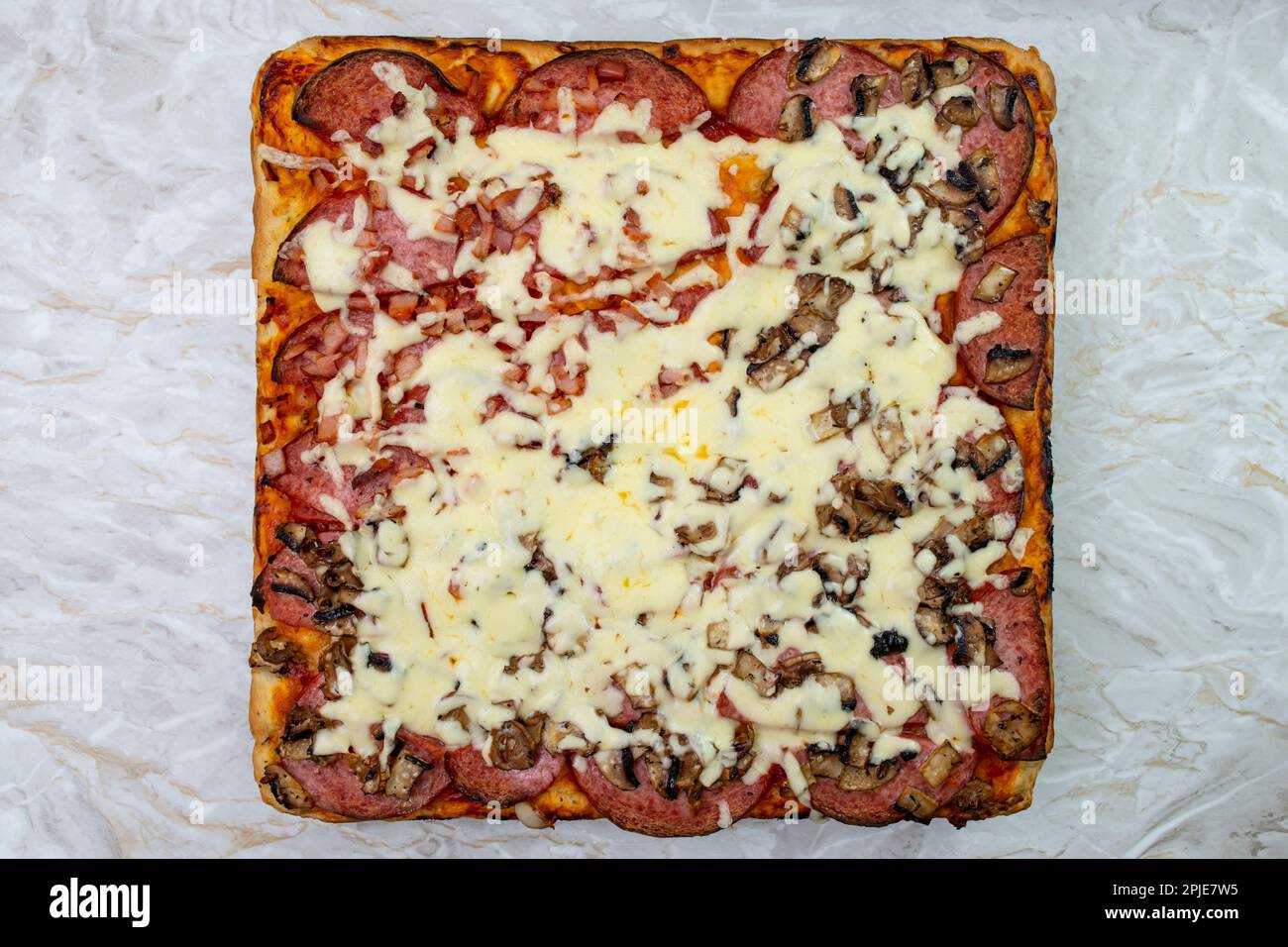 Quadratische Pizza mit Käse und Salami auf weißem Marmorhintergrund, flache Nahaufnahme Stockfoto