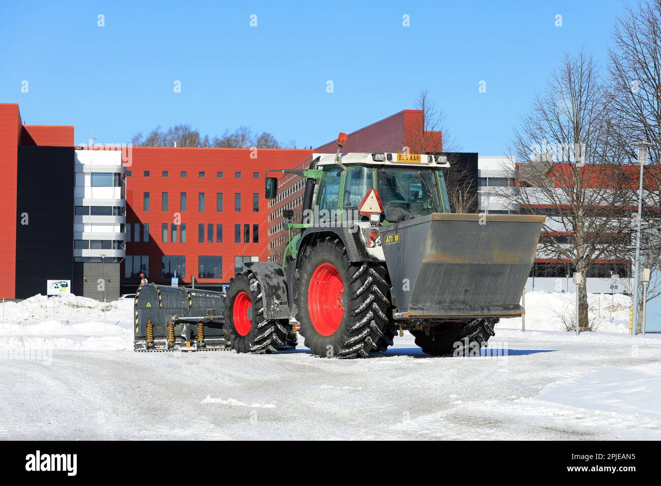 Traktor verteilt Körnung mit ATI 18-Streuer und pflutet Schnee nach Schneefall von der Parkfläche. Rückansicht. Salo, Finnland. 12. März 2023. Stockfoto