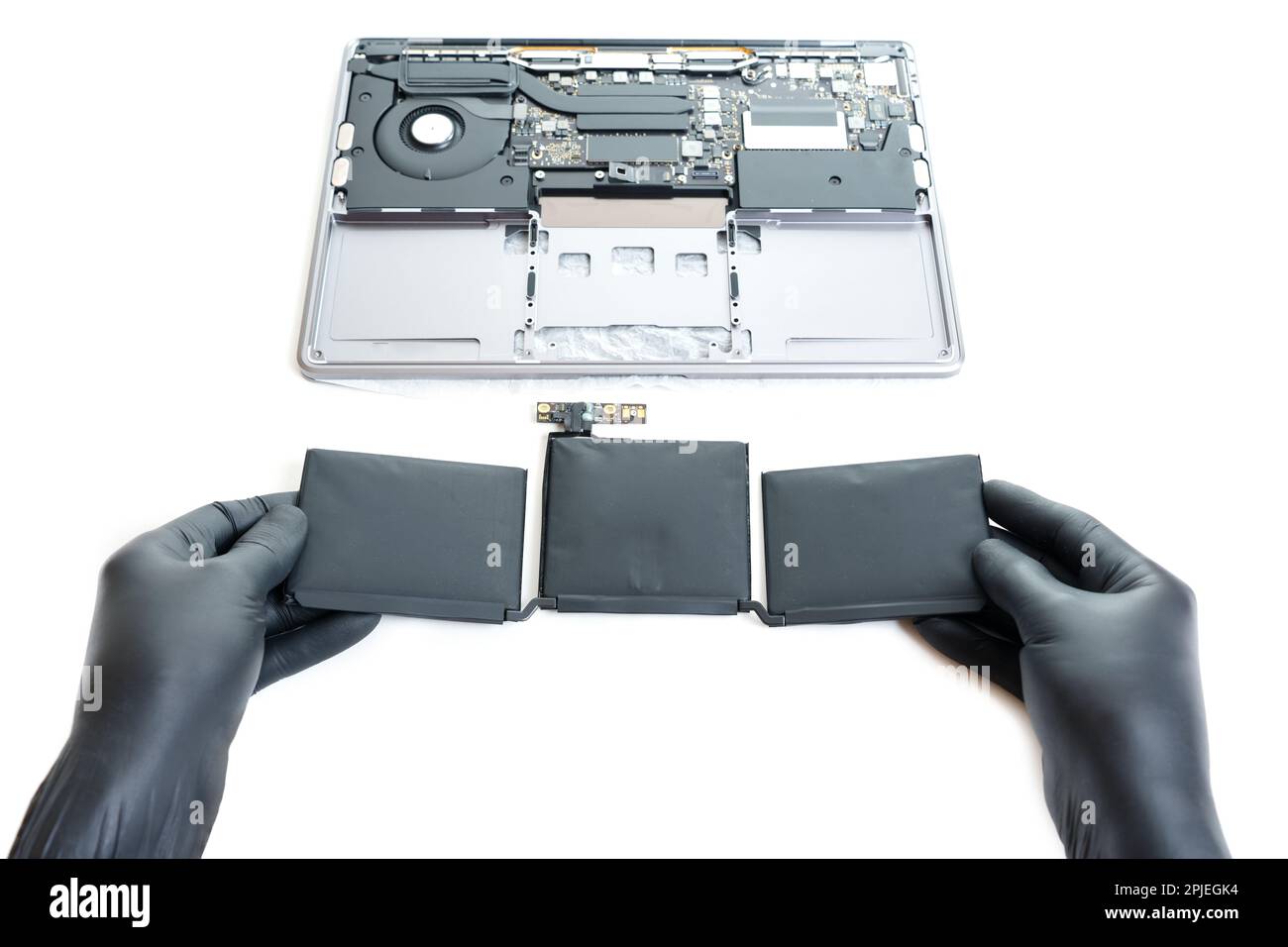 Die Hände in schwarzen Handschuhen halten eine geschwollene Batterie, die gerade aus dem zu reparierenden Laptop entfernt wurde, isoliert auf weiß. Stockfoto