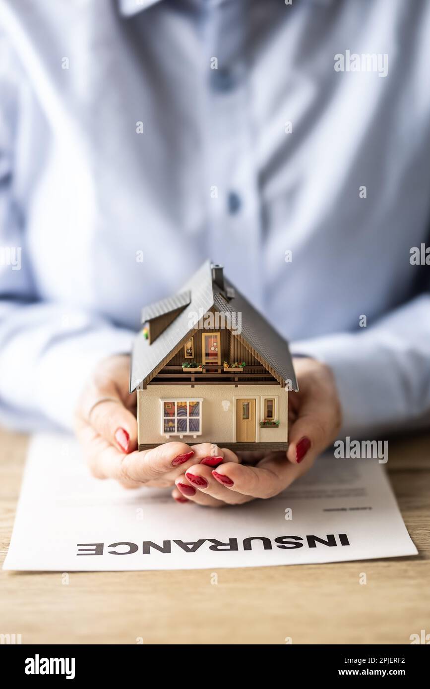 Das Hausversicherungskonzept wird durch weibliche Hände dargestellt, die ein Modell eines Gebäudes auf einem Versicherungsvertrag halten. Stockfoto Das Hausversicherungskonzept wird durch weibliche Hände dargestellt, die ein Modell eines Gebäudes auf einem Versicherungsvertrag halten. Stockfoto