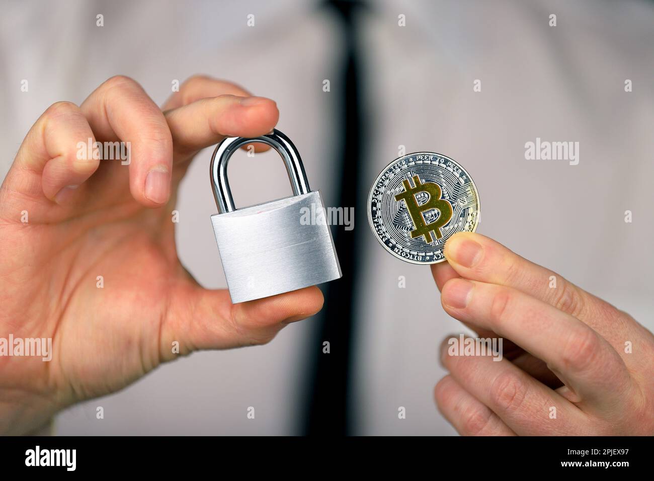 Ein Geschäftsmann hält ein silbernes Vorhängeschloss und eine physische Version von Bitcoins in seinen Händen. Verbot von Kryptowährungen, Vorschriften, Beschränkungen oder Sicherheit Stockfoto