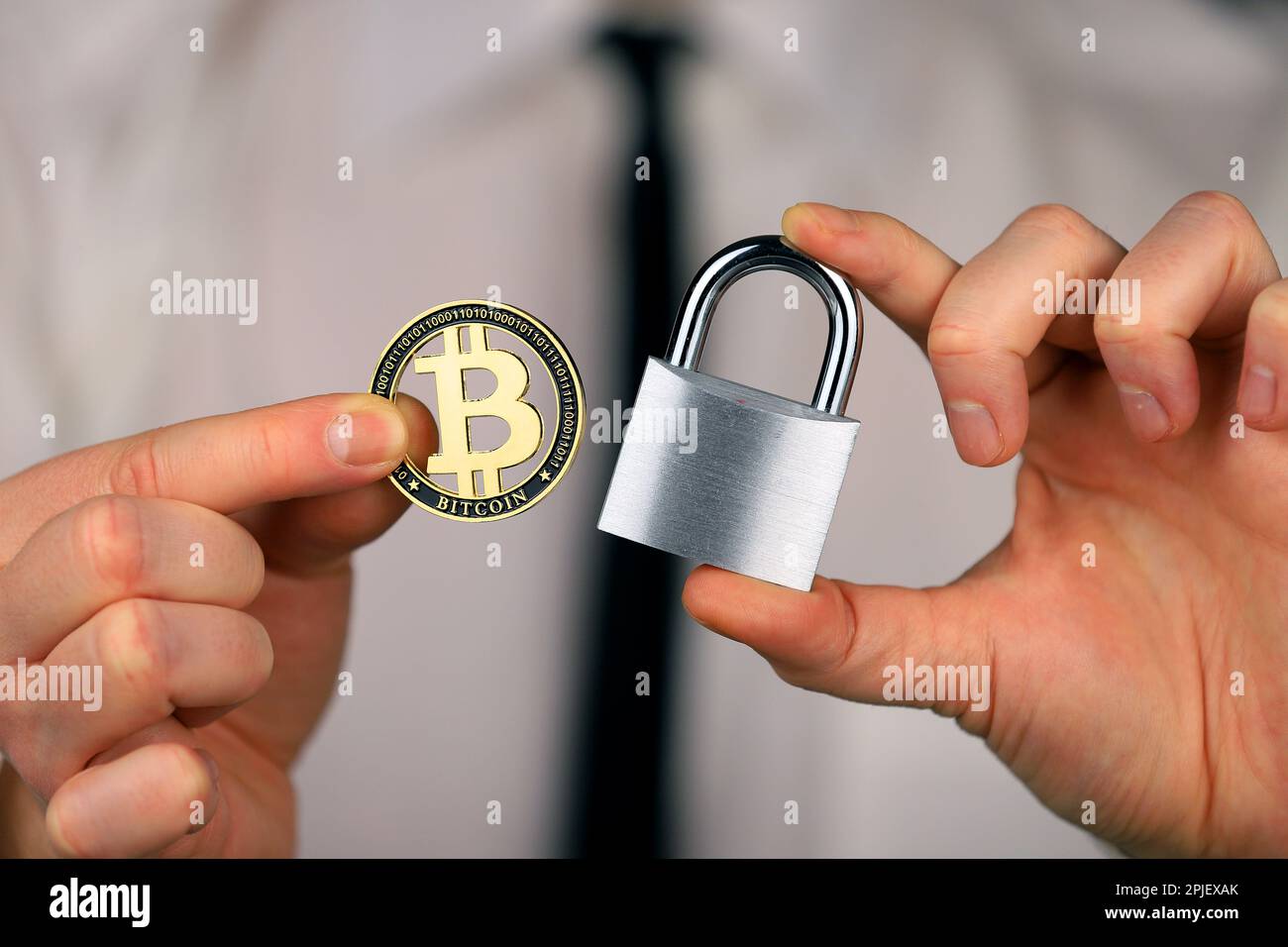 Ein Geschäftsmann hält ein silbernes Vorhängeschloss und eine physische Version von Bitcoins in seinen Händen. Verbot von Kryptowährungen, Vorschriften, Beschränkungen oder Sicherheit Stockfoto