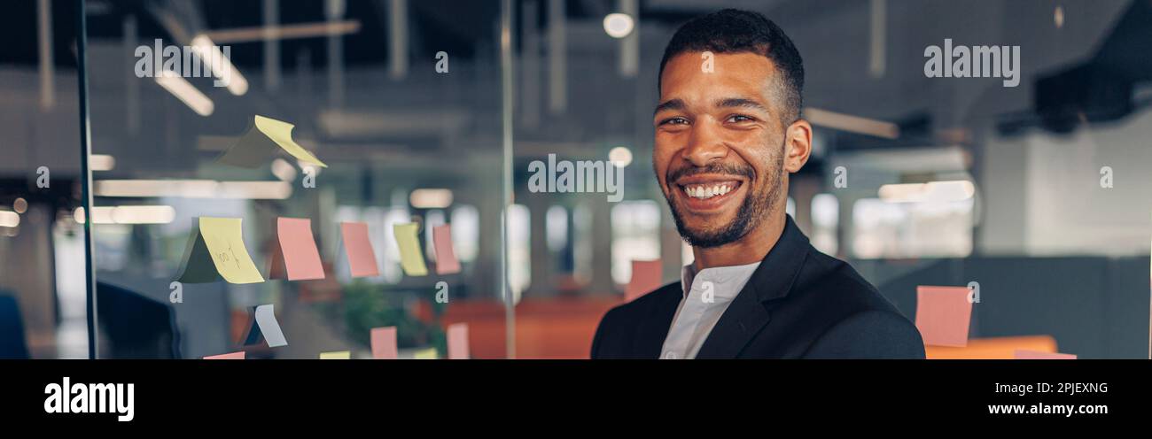 Porträt eines lächelnden afrikanischen Geschäftsmannes, der mit überkreuzten Händen im Büro steht Stockfoto