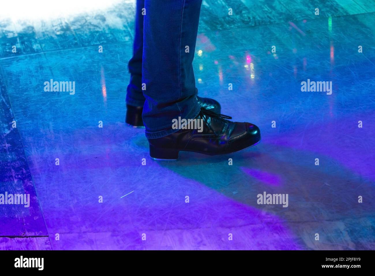 Herrenbeine in Bühnenhose mit Streifen und Lederschuhen für irische Tänze auf dem Boden. Schwarze Arbeitsschuhe für Stepptanz mit Reflexion Stockfoto