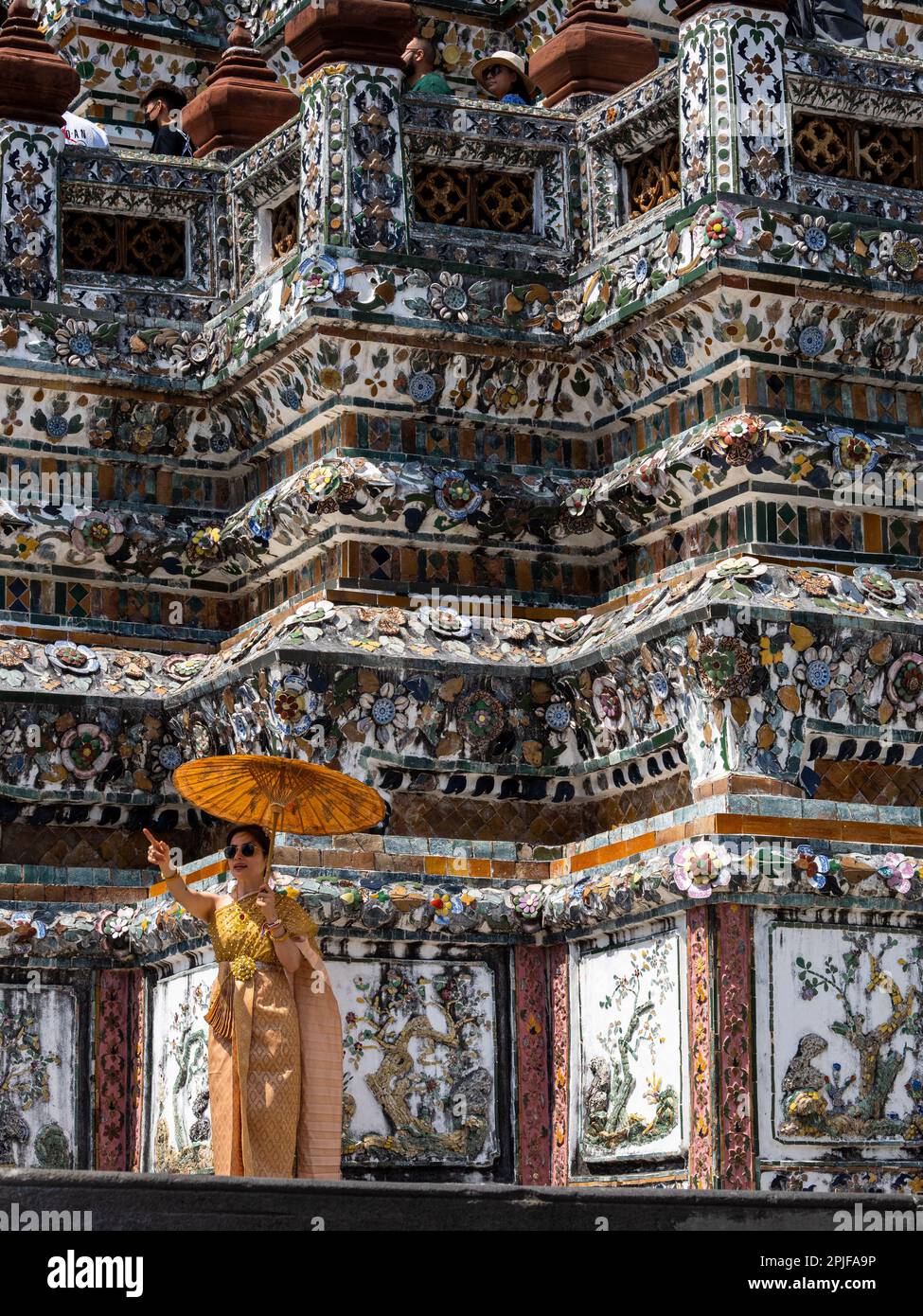 Eine anmutige thailändische Dame in lebendiger orangefarbener traditioneller Kleidung steht stolz auf den herrlichen Wat Arun Tempel in Bangkok, Thailand, mit einer ma Stockfoto