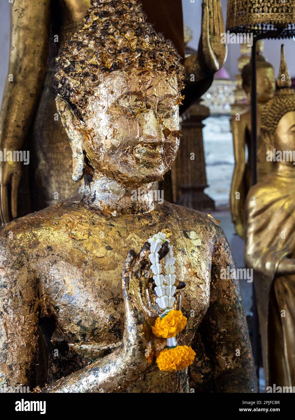 Werfen Sie einen Blick auf die Göttlichkeit mit dieser atemberaubenden Nahaufnahme einer goldenen Buddha-Statue, geschmückt mit einer lebendigen gelben Blume, Phuang Malai, am Wat Arun Tempel i. Stockfoto