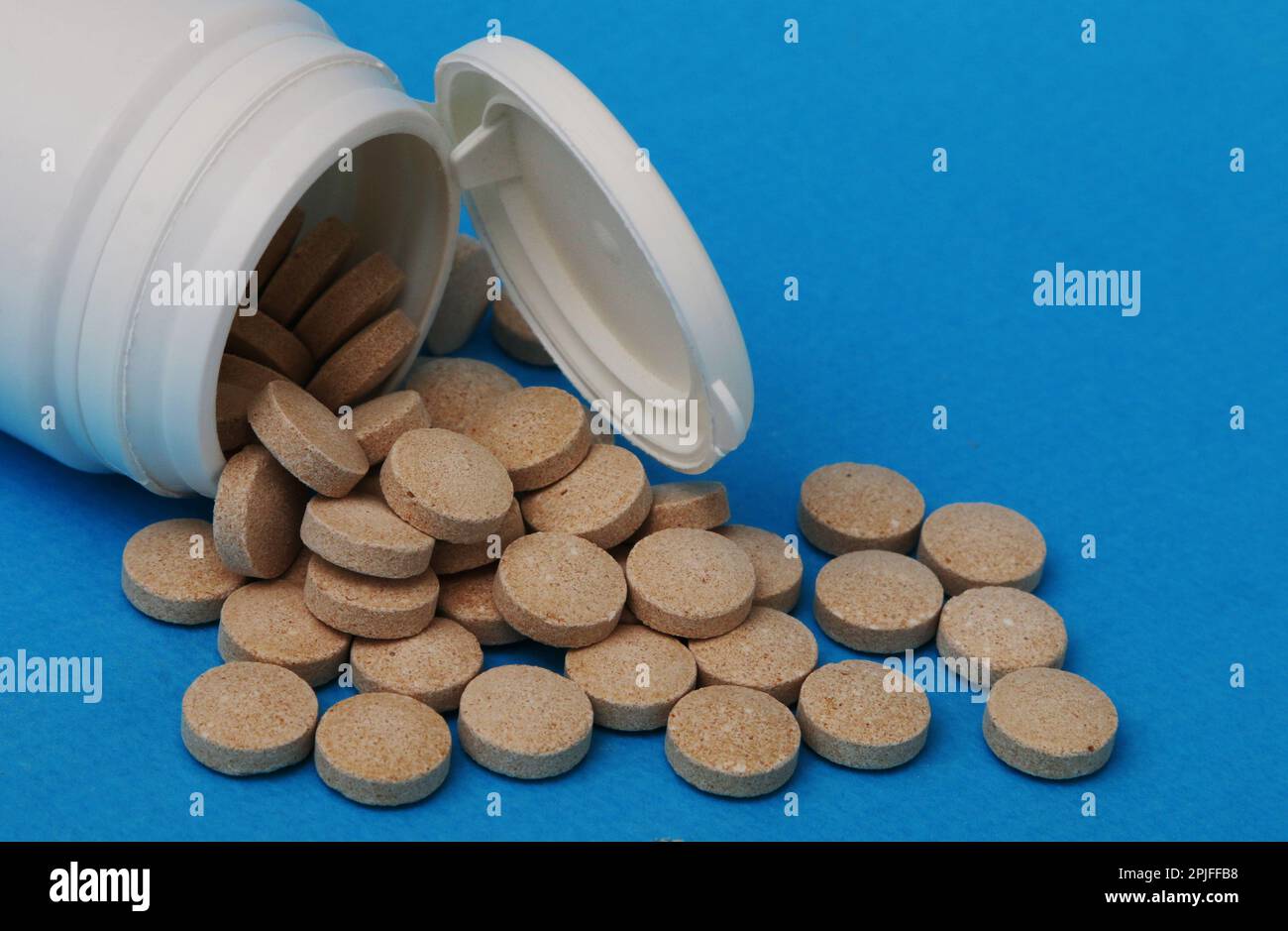 Medizin und Gesundheitskonzept. Gelb-braune Pillen Nahaufnahme. Aus einer weißen Plastikflasche verschüttete Pillen. Stockfoto