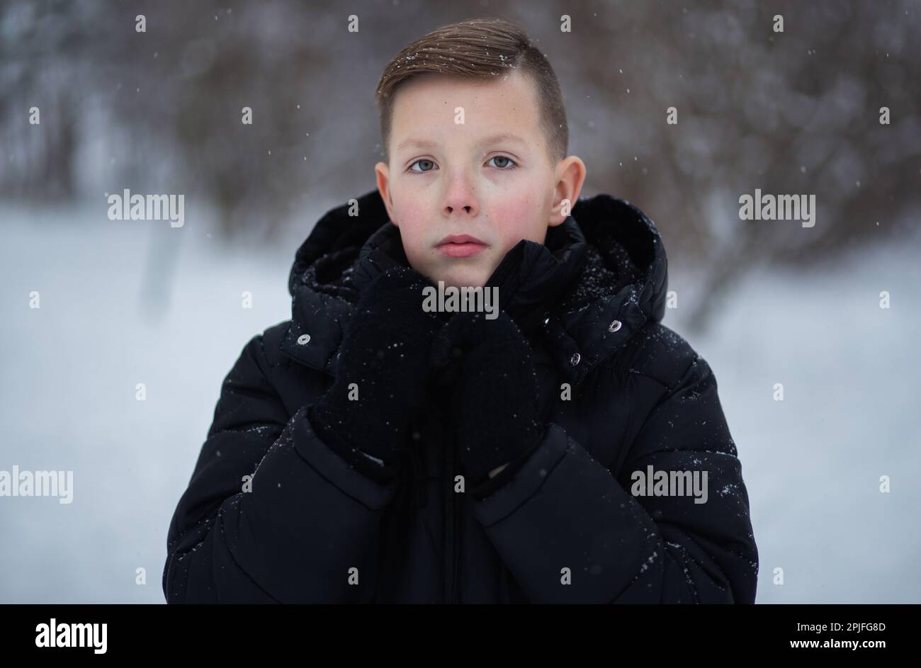 Ein süßer Junge im Alter von 13-15 Jahren in dunkler Winterkleidung und schwarzen Handschuhen im Freien sieht in die Kamera. Stockfoto
