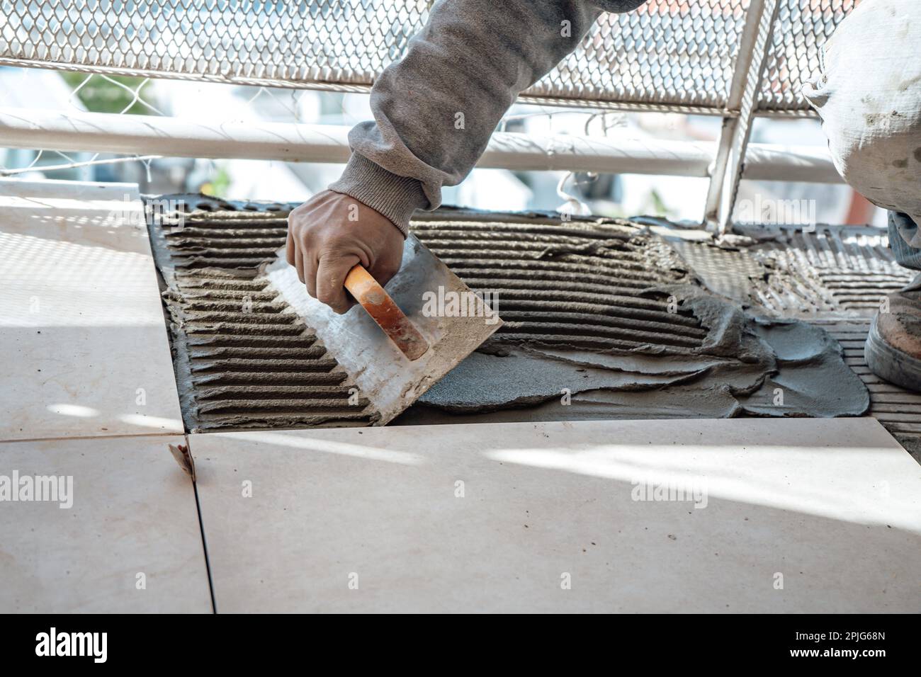 Maurer bereitet Zement auf einer Platte mit einer gekerbten Kelle vor. Ich arbeite in einer Baustelle. Arbeitskonzept, Handel. Stockfoto