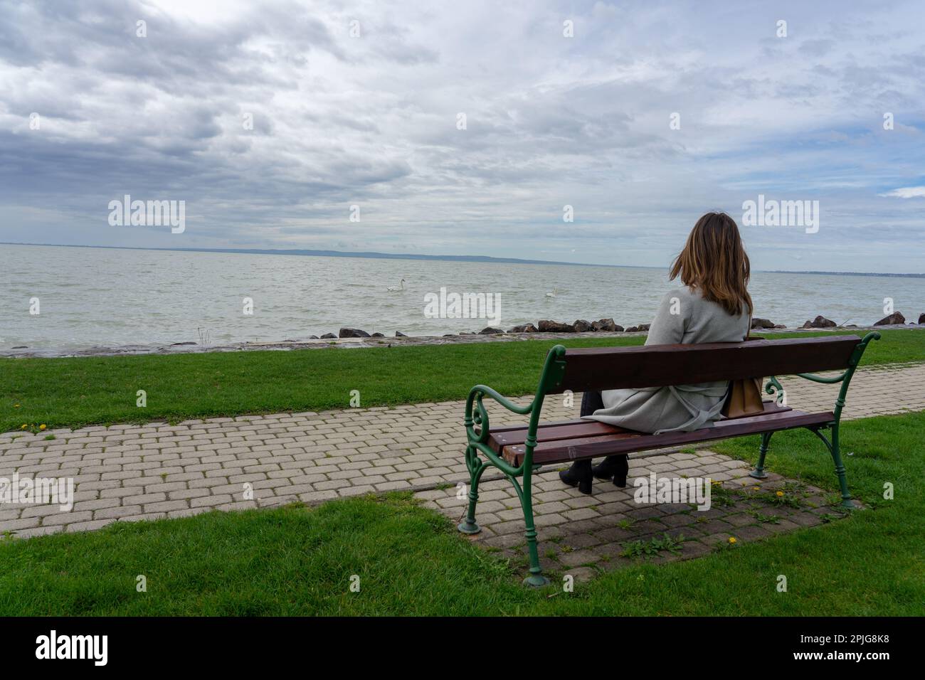 Frau, die im Frühling in Ungarn auf einer Bank am Balaton-See sitzt. Stockfoto