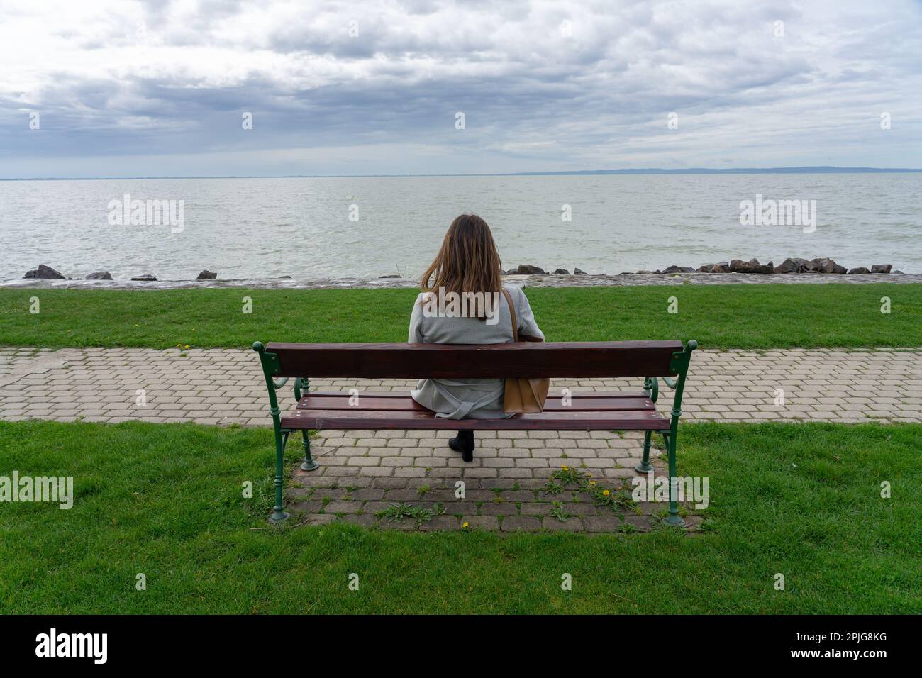 Frau, die im Frühling in Ungarn auf einer Bank am Balaton-See sitzt. Stockfoto