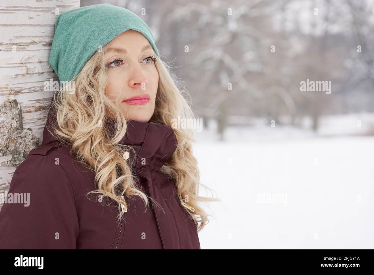 Frau lehnte sich gegen Birke verschneite Winterlandschaft Blick in die Ferne Stockfoto