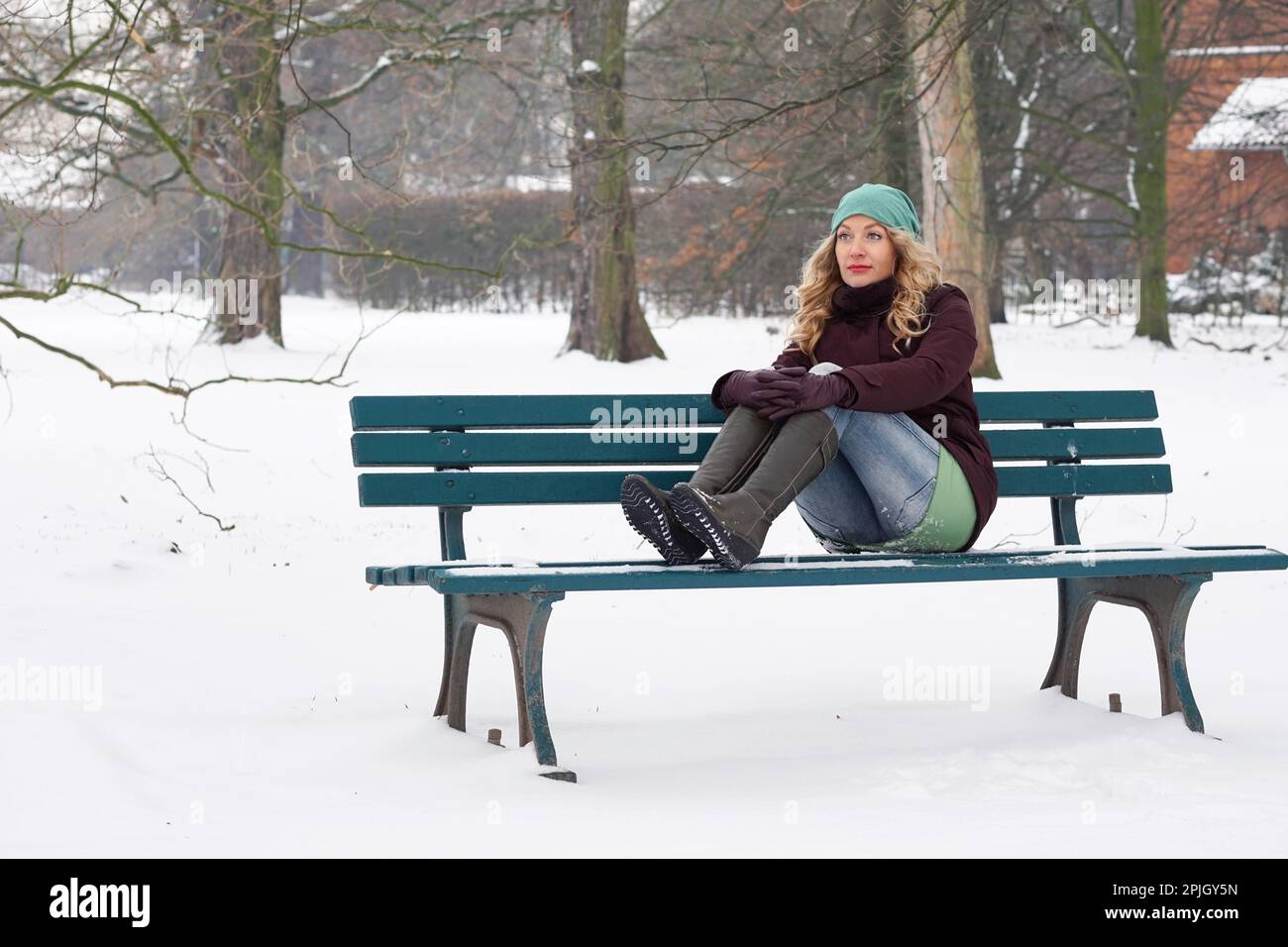 Einsame Frau, die im Winter auf einer schneebedeckten Parkbank sitzt Stockfoto