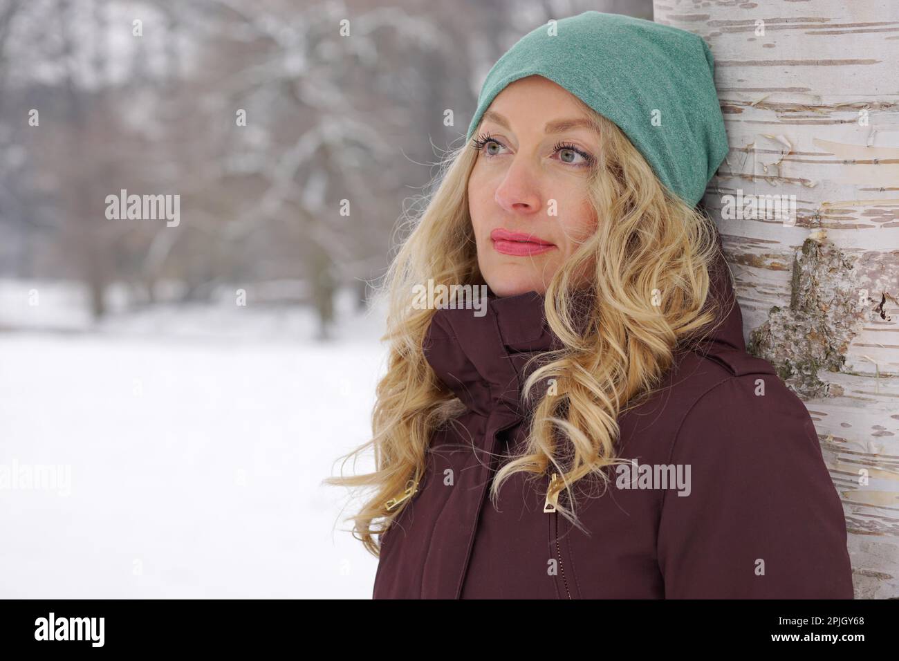 Nachdenkliche Frau lehnte sich gegen Birke verschneite Winterlandschaft Stockfoto