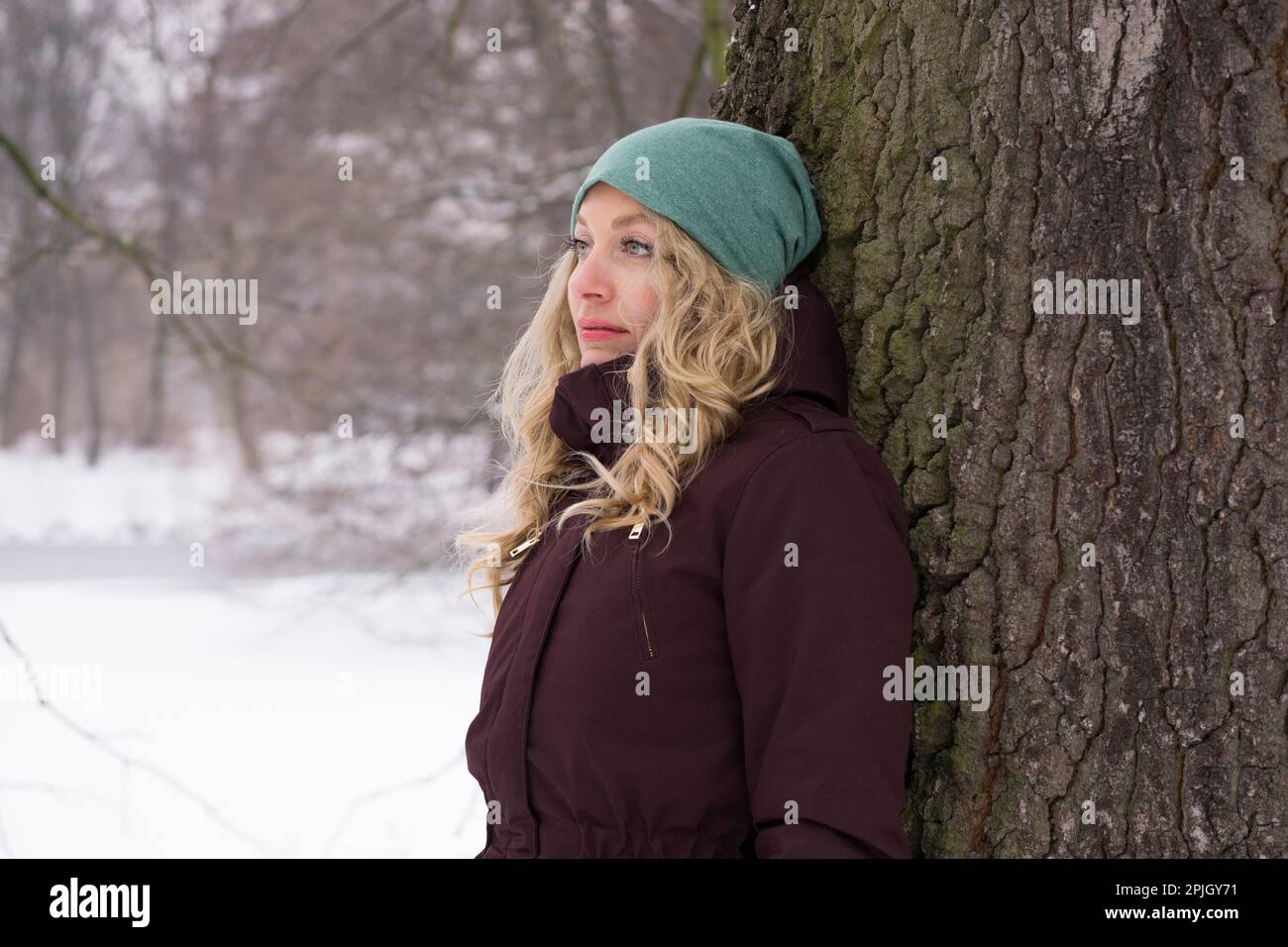 Traurige Frau lehnt sich im Schnee an den Baum und leidet an Winterdepression Stockfoto