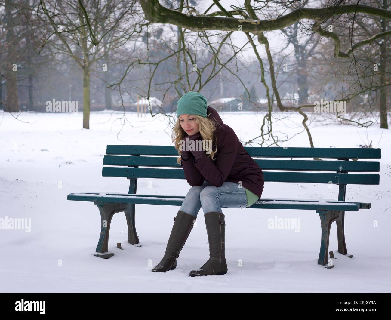 Eine Frau, die allein auf einer schneebedeckten Parkbank mit Winterdepression sitzt Stockfoto