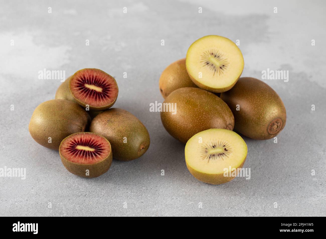Rote und goldene Kiwi, ganz und halbiert auf einem grauen Tisch. Verschiedene Kiwisorten. Stockfoto