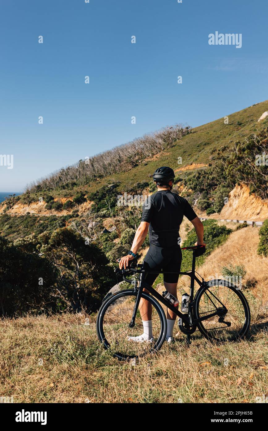 Professioneller Radfahrer in schwarzer Sportbekleidung lehnt sein Fahrrad und schaut auf die Aussicht Stockfoto