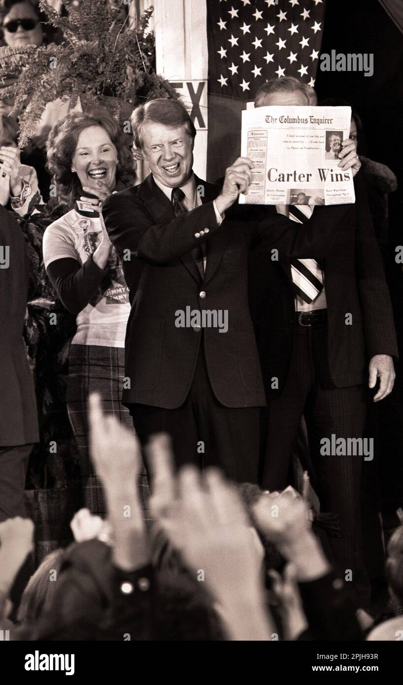 Carter Cousin Betty Pope reagiert, als der designierte Präsident Jimmy Carter eine Zeitung mit der Überschrift „Carter gewinnt“ hält, während er in der Wahlnacht mit Menschenmassen in den Straßen von Tiny Plains, Georgia, feiert. Stockfoto