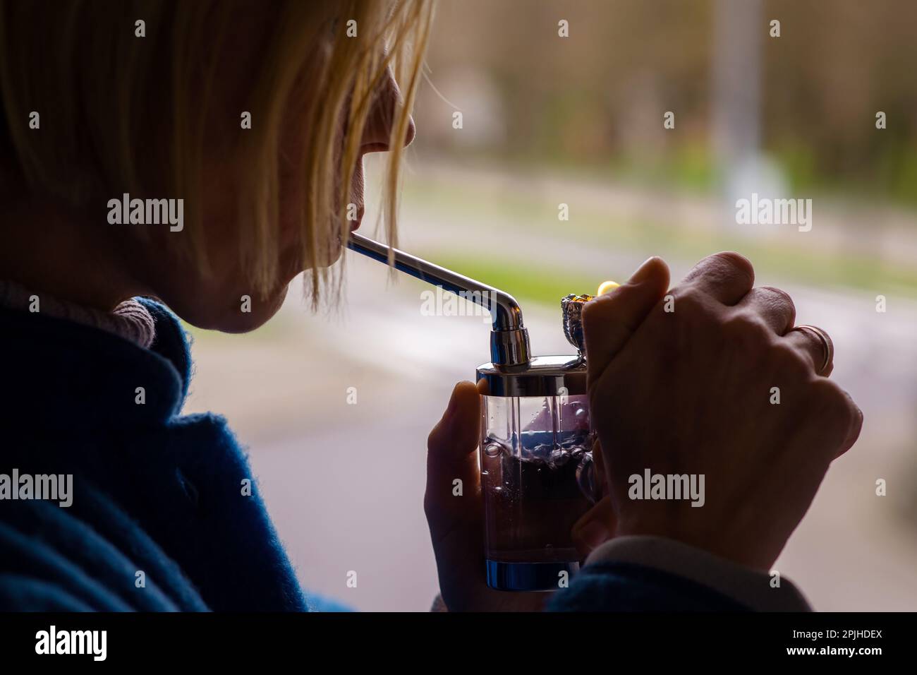 Eine Frau raucht Marihuana, Cannabis. Eine Erwachsene Frau mit blonden Haaren zündet ein Rauchergerät an. Entspannung, ärztliche Verschreibung. Stockfoto