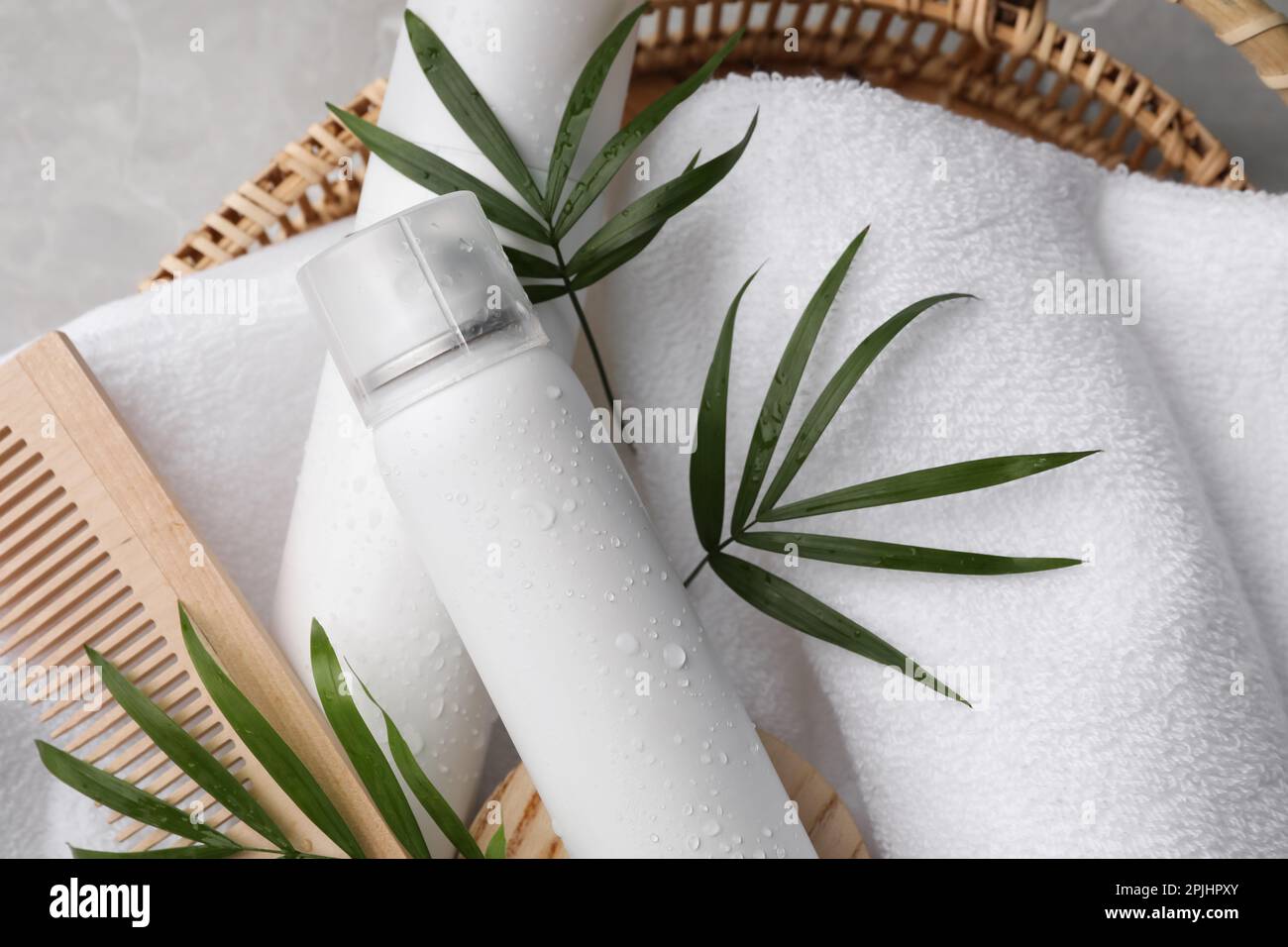 Trockene Shampoo-Sprays, Handtuch und Holzkamm mit grünen Blättern im Korb auf dem Tisch, Draufsicht Stockfoto