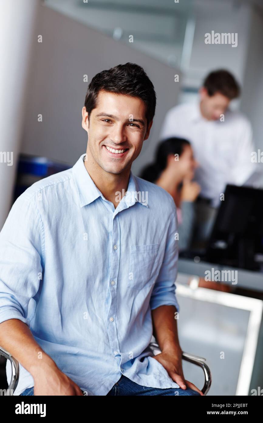 Er ist glücklich, wo er ist. Porträt eines selbstbewussten jungen Geschäftsmannes mit seinen Kollegen verschwommen im Hintergrund. Stockfoto