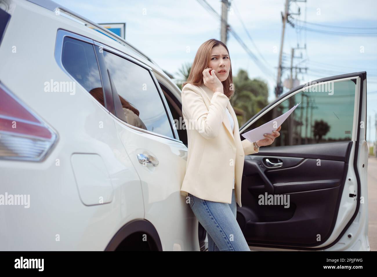 Unzufriedene Geschäftsfrau, die neben einem Auto steht und ein Dokument hält und ein Mobiltelefon benutzt. Stockfoto