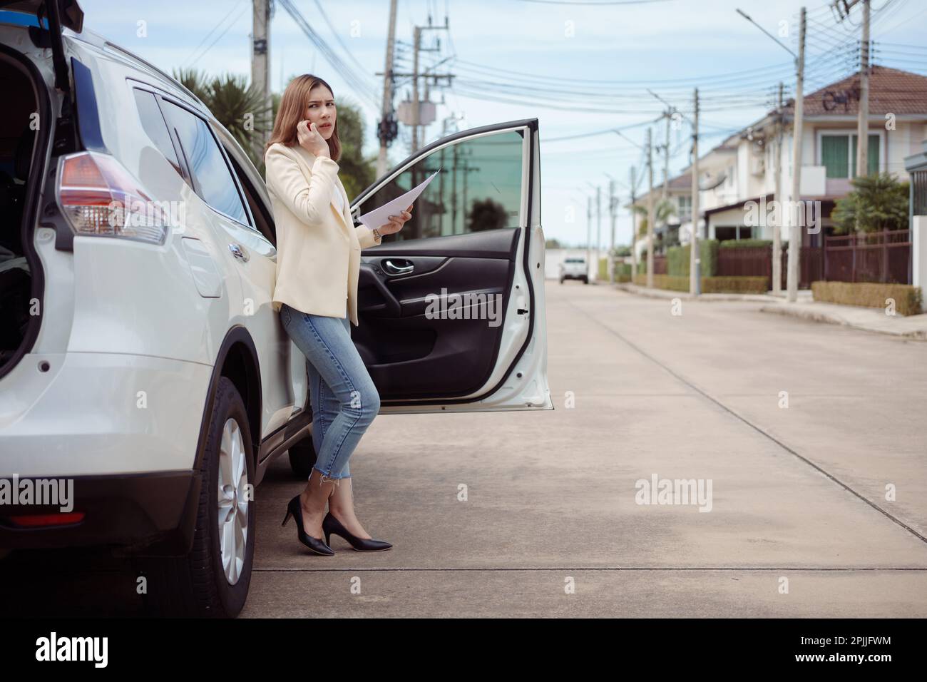 Unzufriedene Geschäftsfrau, die neben einem Auto steht und ein Dokument hält und ein Mobiltelefon benutzt. Stockfoto