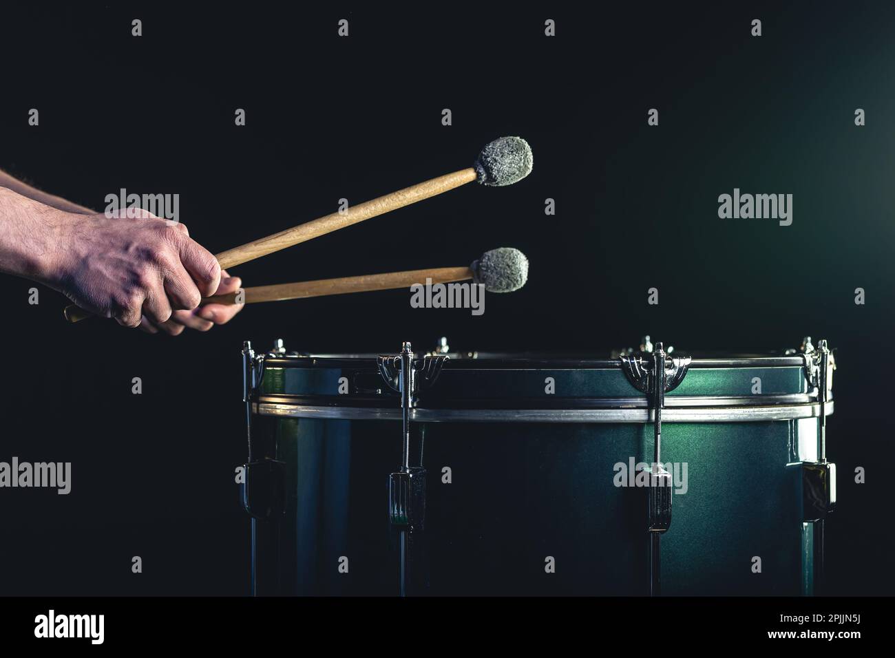 Ein Mann spielt ein musikalisches Schlaginstrument mit Stöcken auf dunklem Hintergrund. Stockfoto