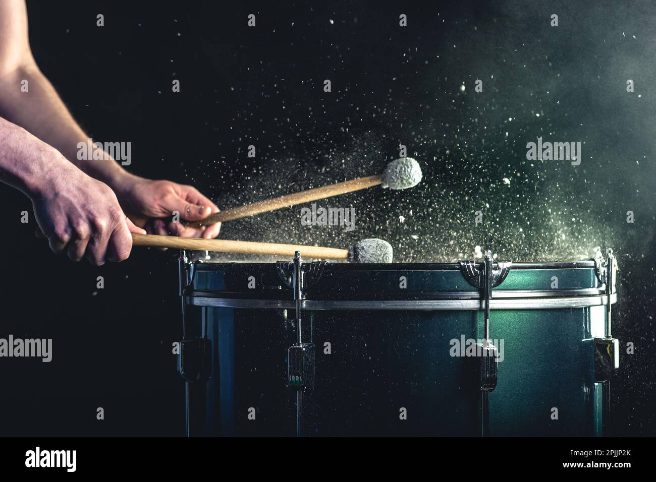 Ein Mann spielt ein musikalisches Schlaginstrument mit Stöcken auf dunklem Hintergrund. Stockfoto