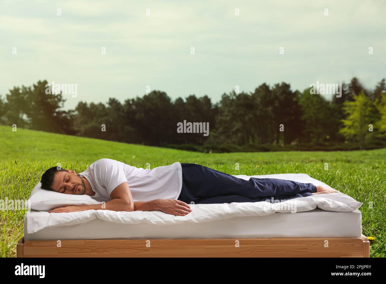 Mann schläft auf dem Bett und wunderschöner Blick auf den grünen Rasen im Hintergrund. Gut schlafen - gesund bleiben Stockfoto