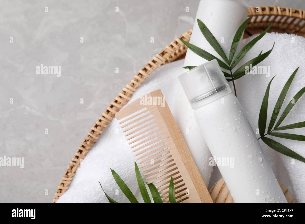 Trockenshampoo-Sprays, Handtuch und Holzkamm mit grünen Blättern im Korb auf hellgrauem Tisch, Draufsicht. Platz für Text Stockfoto
