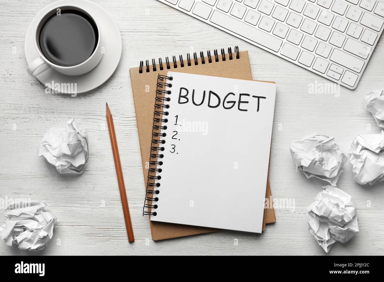 Notizbuch mit Wort Budget und zerknitterten Papierkugeln auf weißem Holztisch, flach liegend Stockfoto