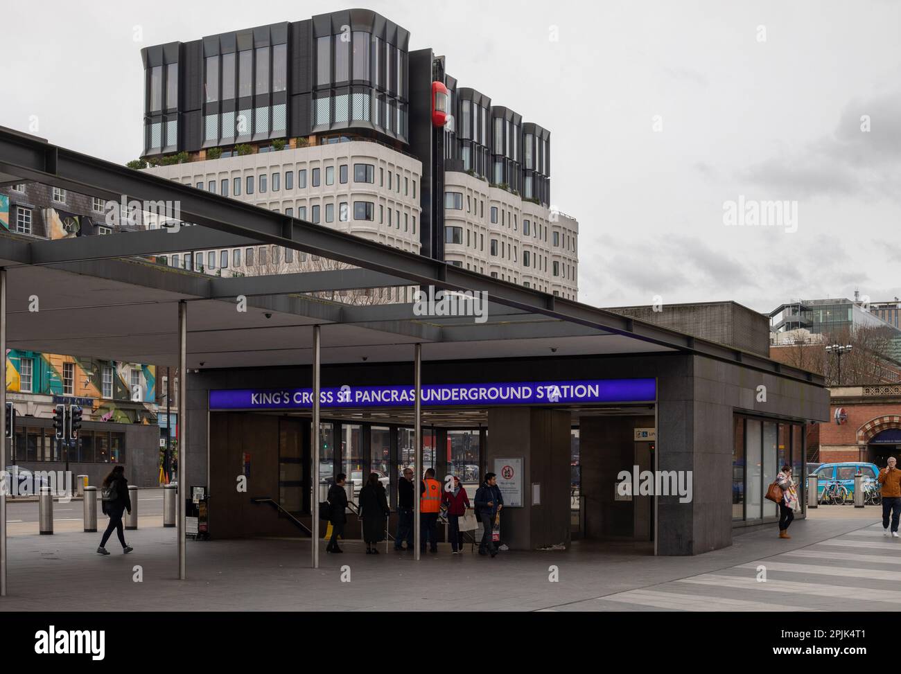 Die Menschen betreten und verlassen die King's Cross St. Pancras U-Bahnstation an einem bewölkten Tag. Dahinter befindet sich das Gebäude des Standard Hotels. Stockfoto